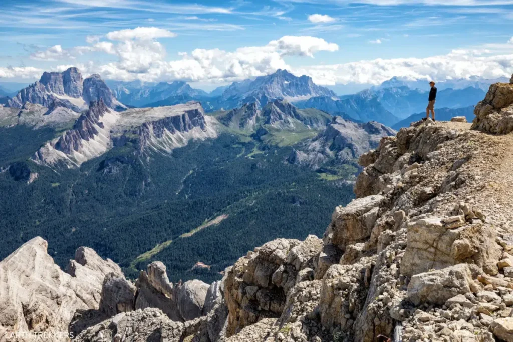 Dark blue mountains dark gren forests on   left side and gray gorge landscpage hill on right side a man standing on this cliff in Cima Tofana Dolomites in a Trip to Dolomities Matera Bari